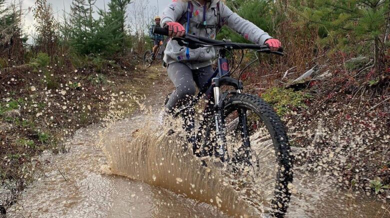 young girl mountain biking on a trail through a puddle
