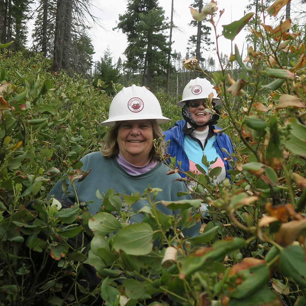 two women with hardhats in the bushes smiling